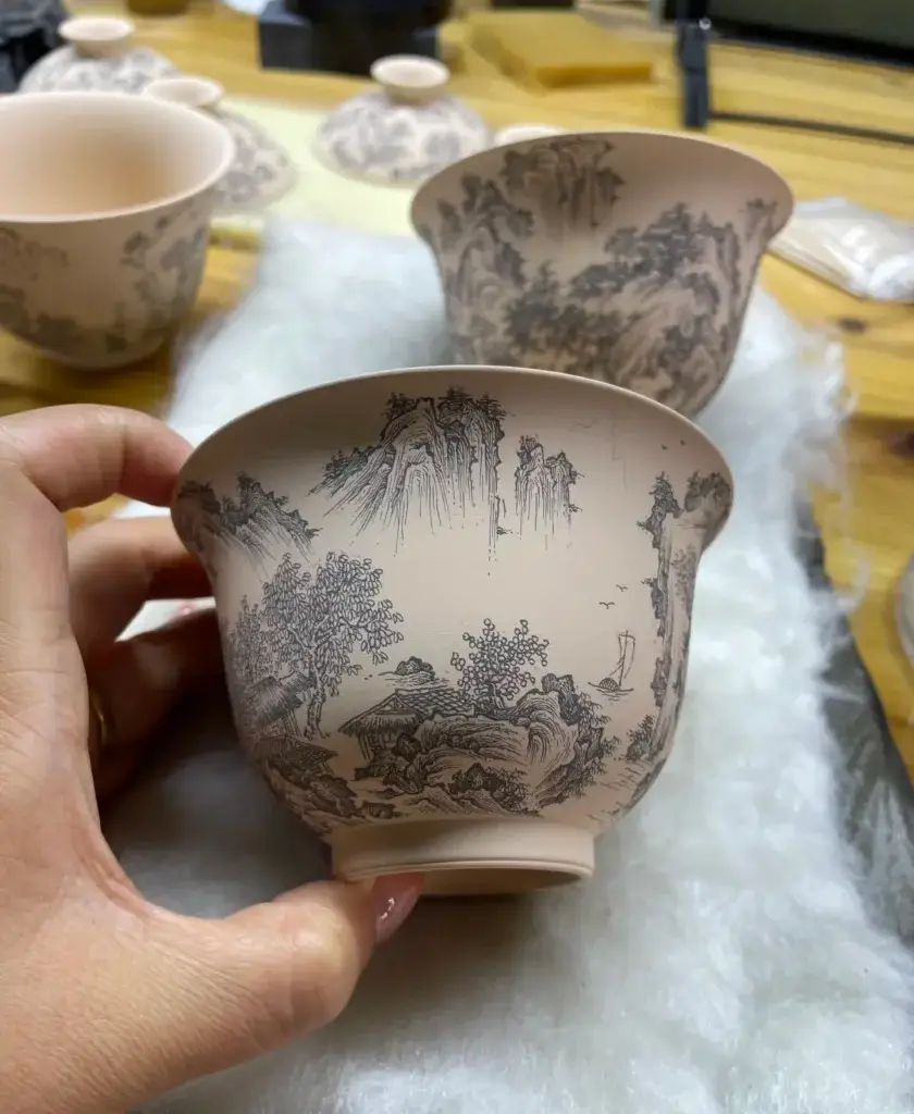 Artisan at work: hand-painting landscape design on unglazed porcelain, showcasing the creative process