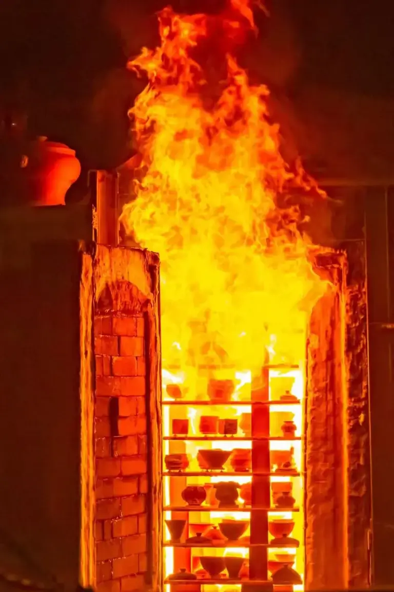 Wood-fired kiln firing handmade Chinese porcelain teacup with glowing fiery light